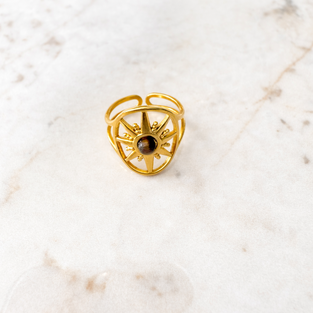 Bague étoile dorée avec au centre pierre oeil de tigre, posée sur surface en marbre clair