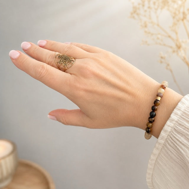 Main de femme Astrid HERMELIN De A à KÂ portant un bracelet lithothérapie chakra plexus solaire Omsaé avec bague métathron, chemisier ivoire, gypsophyle et bougie