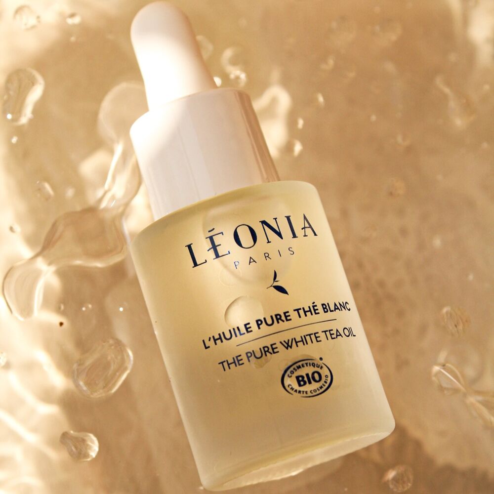 Flacon compte gouttes Léonia Paris L'Huile Pure Thé Blanc Bio, huile visage régénérante certifiée cosmétique bio, posé sur fond doré avec texture