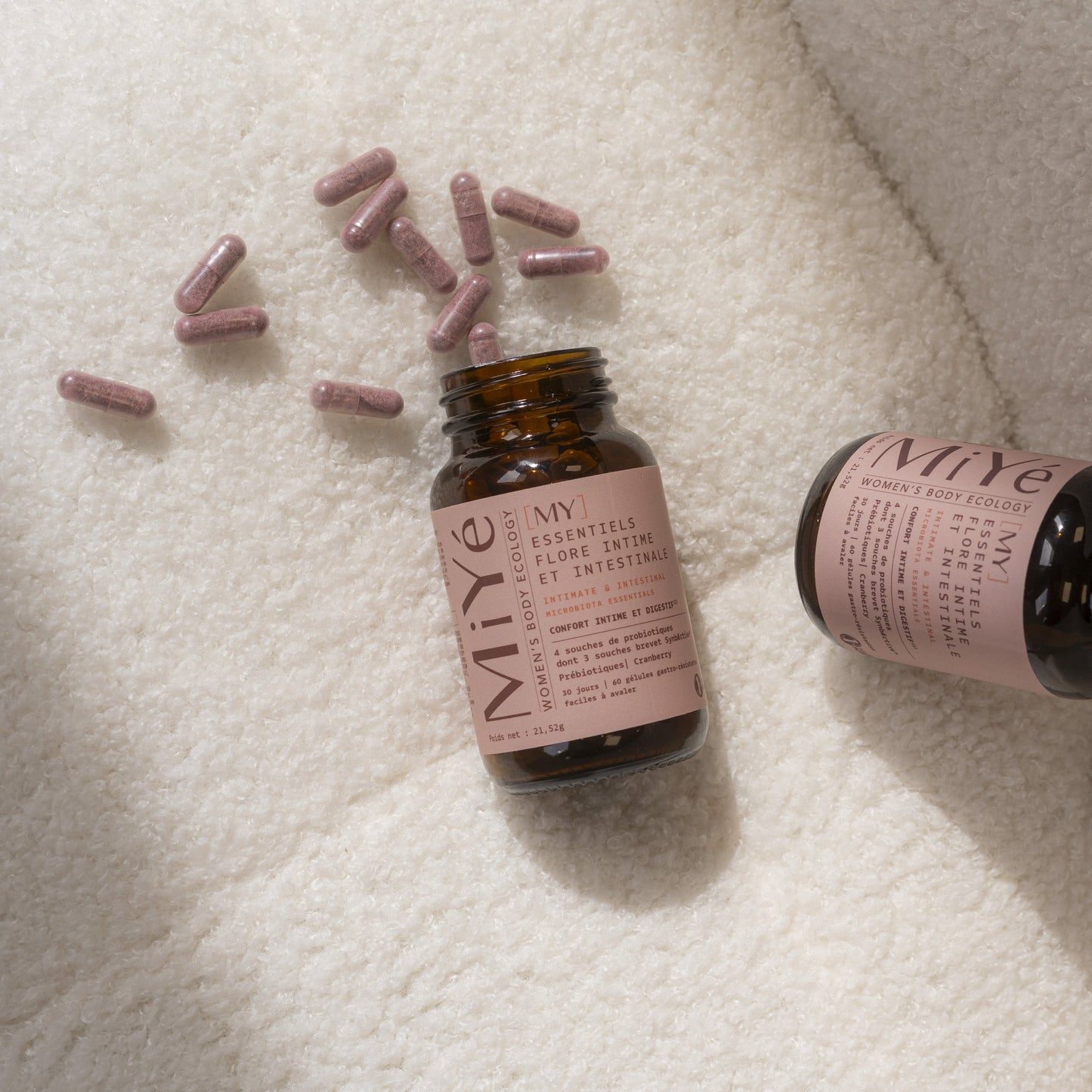 Deux flacons en verre brun avec étiquette rose du complément alimentaire My essentiels flore intime et intestinale MiYé avec des gélules roses sur fond ivoire