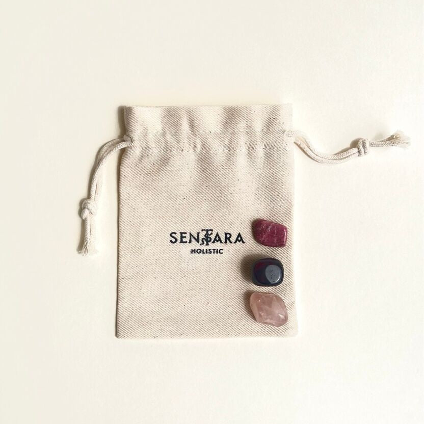3 pierres roulées de quartz rose, rhodonite et grenat rouge pour kit amour lithothérapie, posées sur pochon en coton ivoire, marque Sentara Holistic en noir