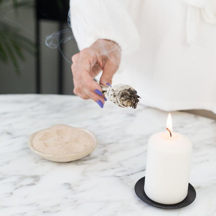 Bâtonnet de sauge blanche allumé dans une main de femme approchant d'une bougie