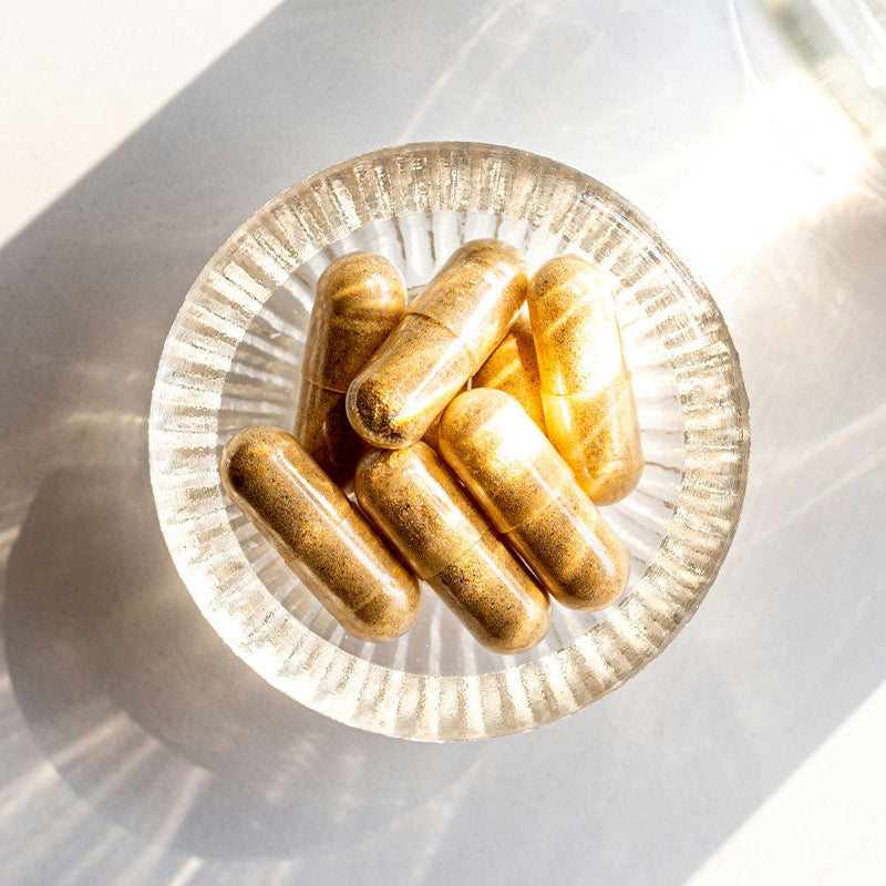 Gélules beiges posées dans une coupelle en verre, sur fond lumineux et minimaliste, ambiance naturelle et épurée