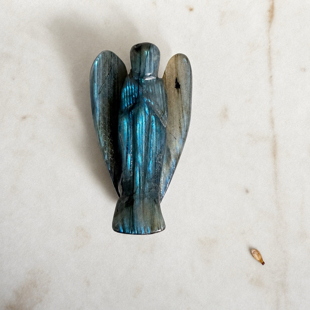 Petit ange en labradorite grise aux reflets verts sur fond marbre clair