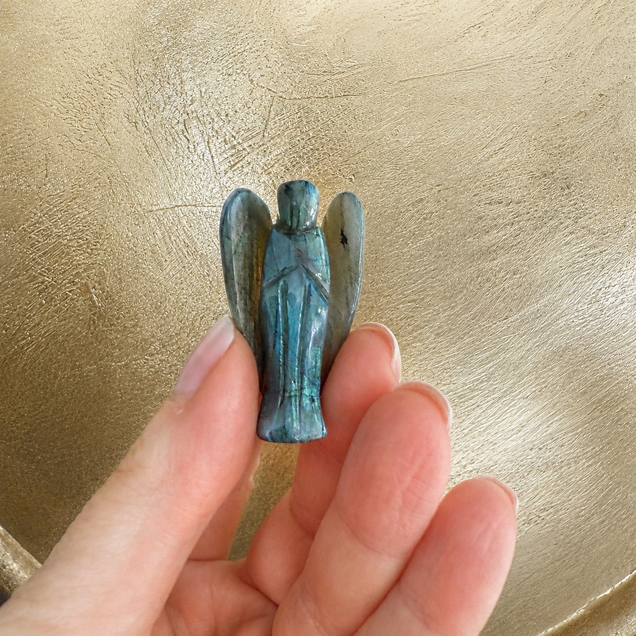 Main tenant une figurine ange en labradorite grise sur fond métal doré