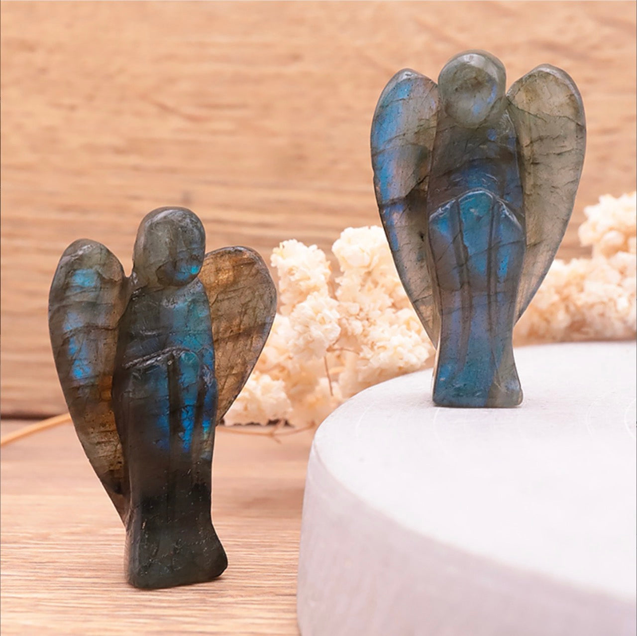 2 anges taillés en pierre naturelle de labradorite grise aux reflets verts, sur bois clair et socle béton blanc avec fleurs séchées