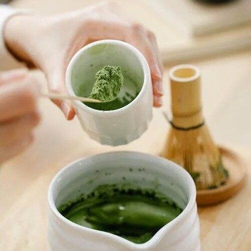 Mains de femme préparant un thé matcha, poudre verte, cuillère doseuse bois, chasen