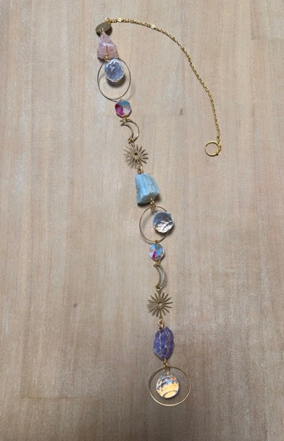 Attrape soleil posé sur une table en bois avec sa chaine en métal doré, ses symboles de lune et soleil , ses pierres naturelle