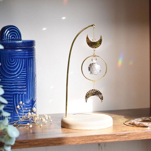 Attrape-soleil Luna Omsaé, en laiton doré cristal facetté, deux lunes, socle en bois,  posé sur une étagère 