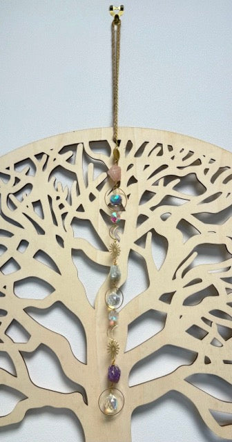 Attrape soleil avec chaine et symbole lune et soleil en métal doré avec ses pierres naturelles, devant un arbre de vie en bois