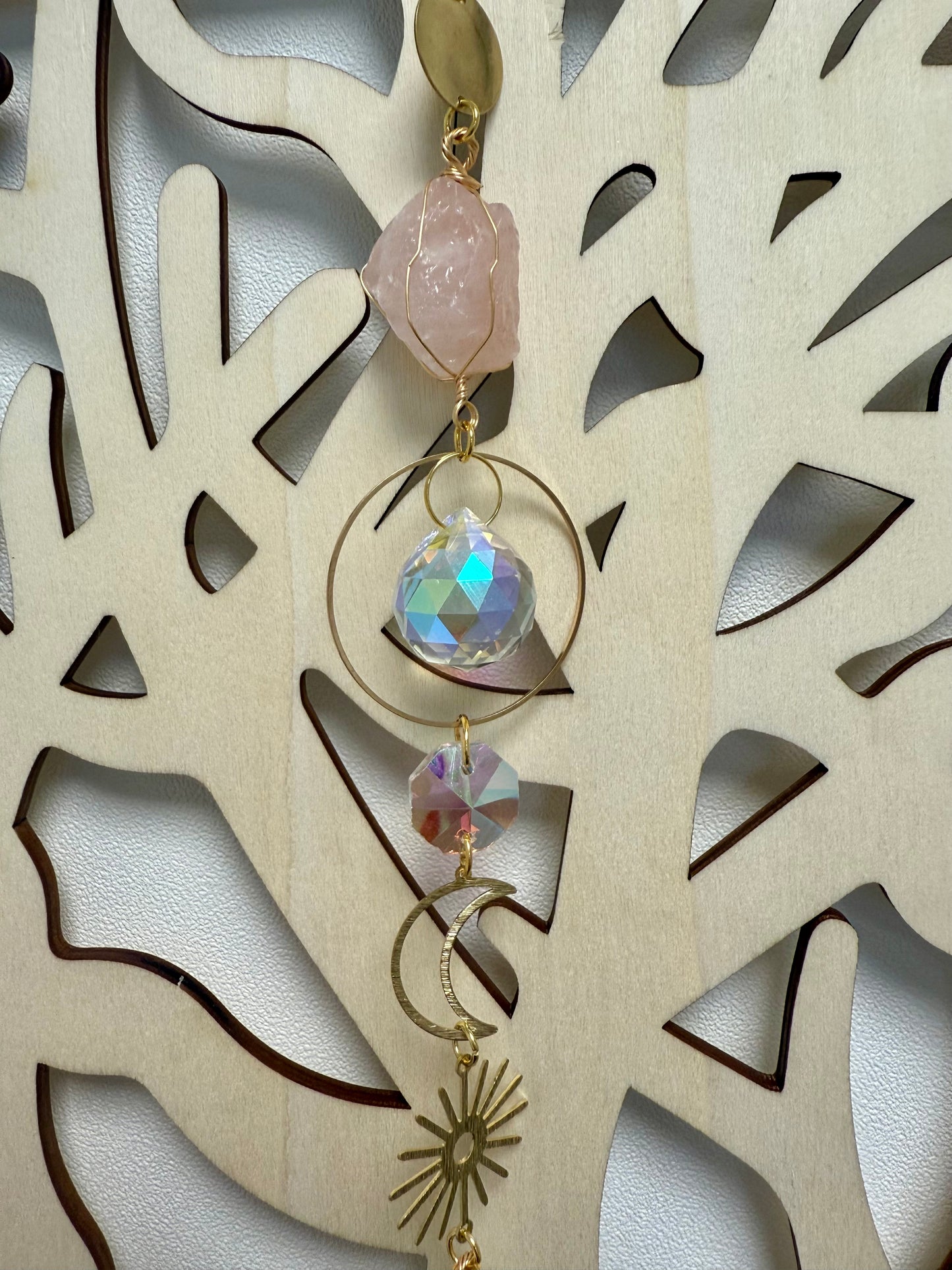 Gros plan sur une partie d'un attrape soleil en métal doré et pierres naturelles devant un arbre de vie en bois clair