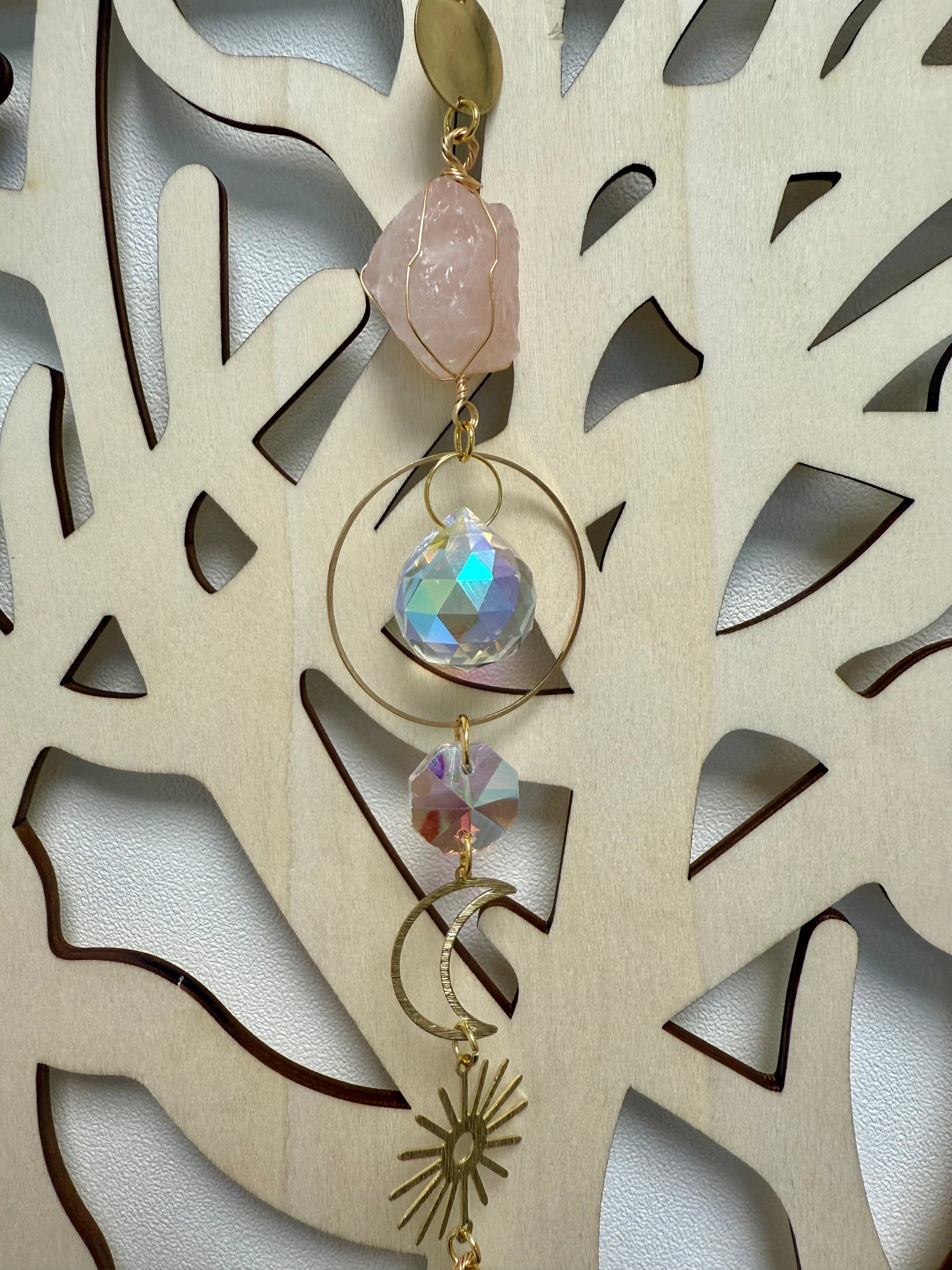 Gros plan sur une partie d'un attrape soleil en métal doré et pierres naturelles devant un arbre de vie en bois clair