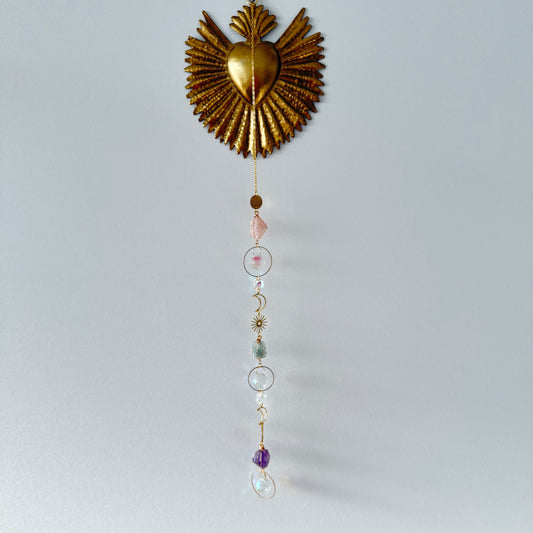Sacré coeur or accroché sur un mur blanc avec attrape soleil doré, cristal de roche, quartz rose, améthyste, fluorite, lune et soleil