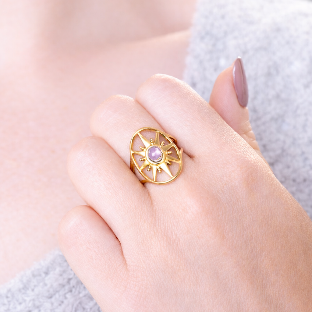 Bague dorée en forme d'étoile avec améthyste au centre, portée par une main de femme
