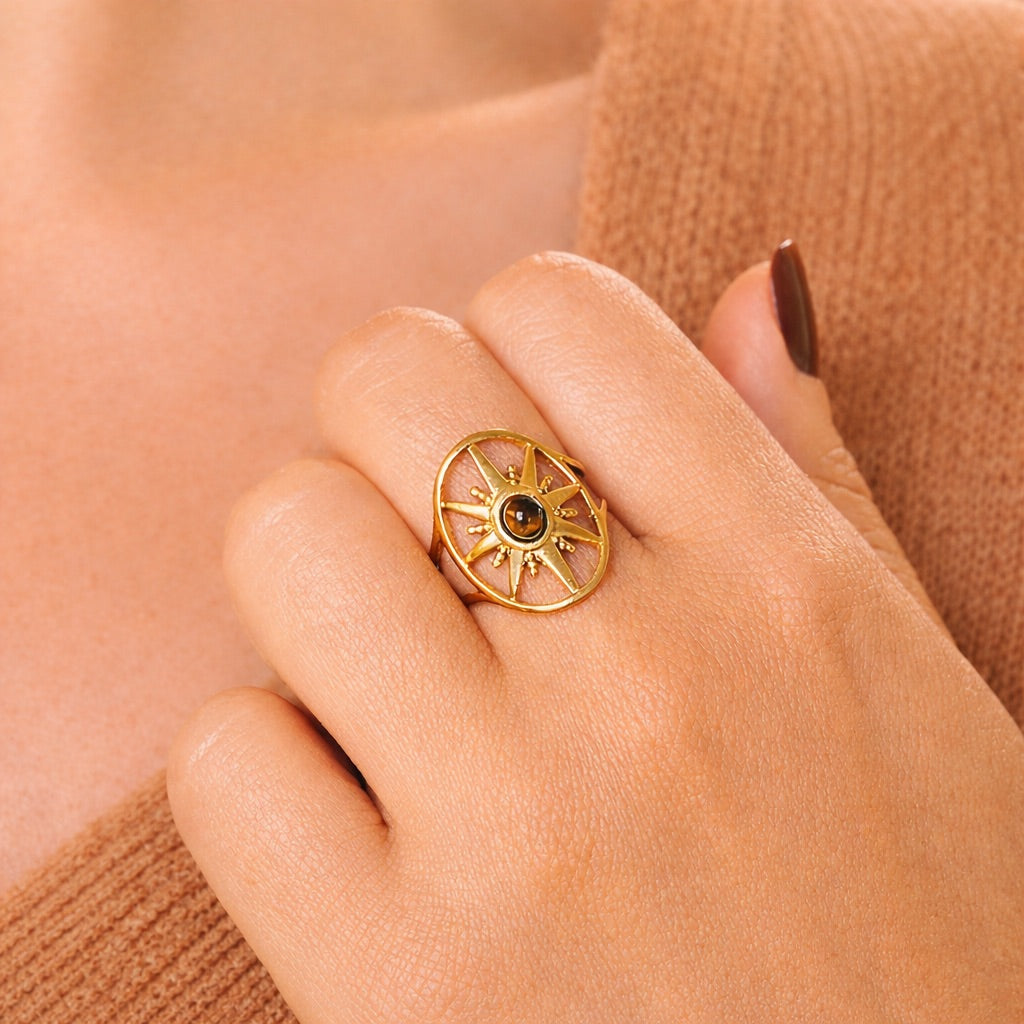 Main de femme avec vernis marron et bague dorée en forme d'étoile avec pierre d'oeil de tigre au centre, pullover camel
