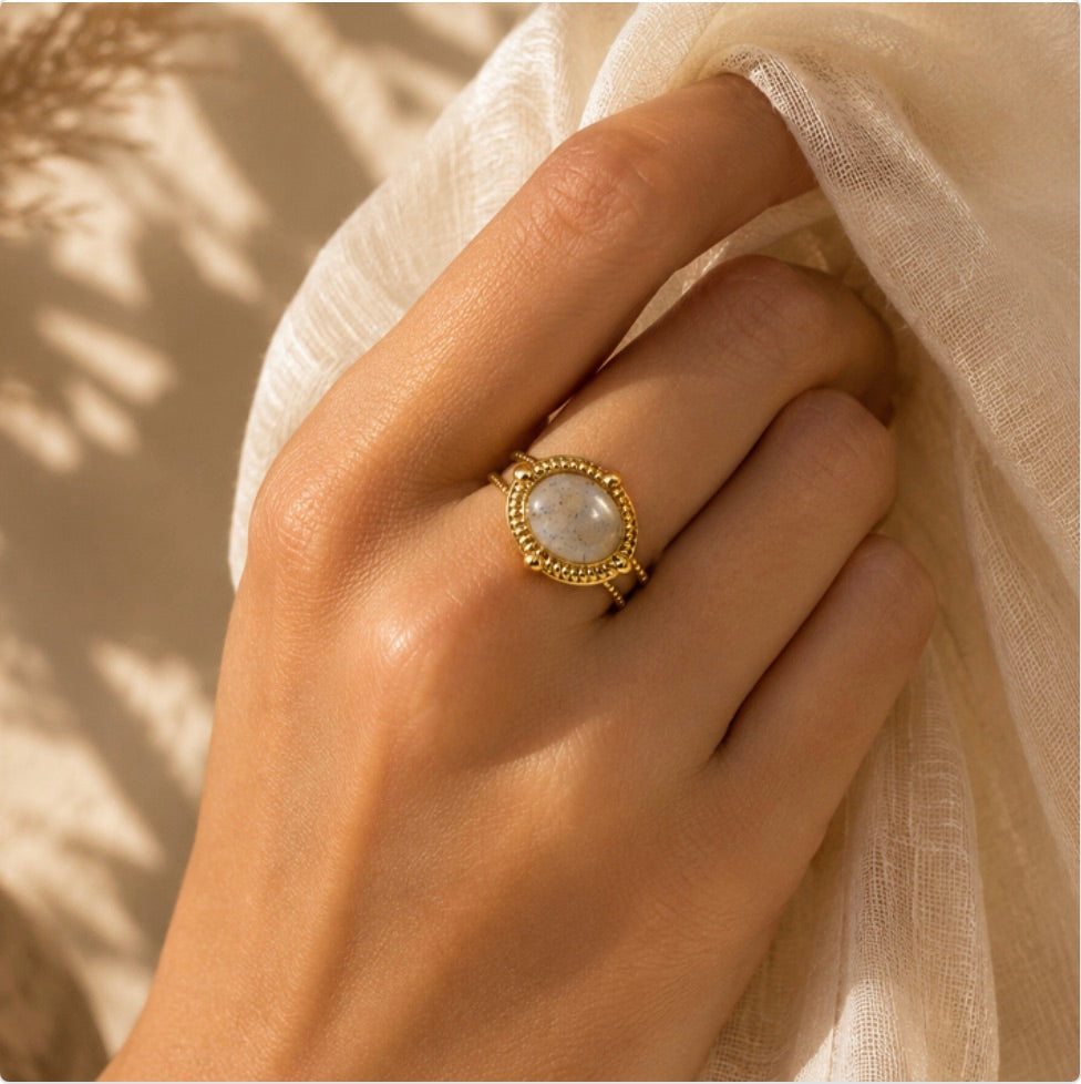 Bague Sahira dorée en labradorite portée sur une main près d’un tissu en lin ivoire
