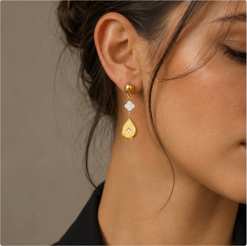 Boucle d’oreille dorée portée à l’oreille, avec charm blanc en nacre et pendentif en forme de goutte orné d’une pierre de zircon