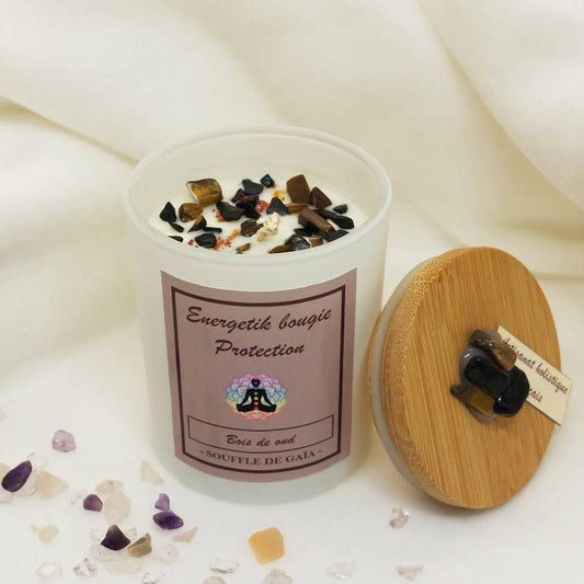 Bougie énergétique Bois de Oud avec cristaux, feuilles d'or, plantes et sont couvercle en bambou posé à côté, fond tissu ivoire