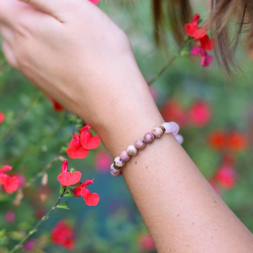 Main de femmes dans la nature avec des fleurs rouges et un bracelet en perles de pierres naturelles,  quartz rose, rhodonite, rhodochrosite