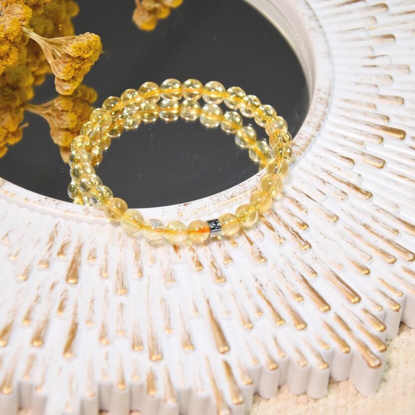 Bracelet élastique en perles de citrine jaune, posé sur un miroir encadré de bois et fleurs séchées jaunes
