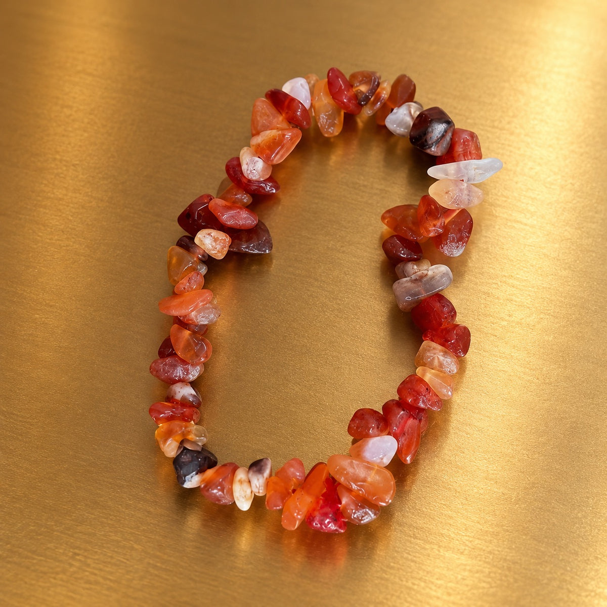 Bracelet en éclats de cristaux de cornaline aux nuances orangées, rouges et translucides, disposé sur un fond doré