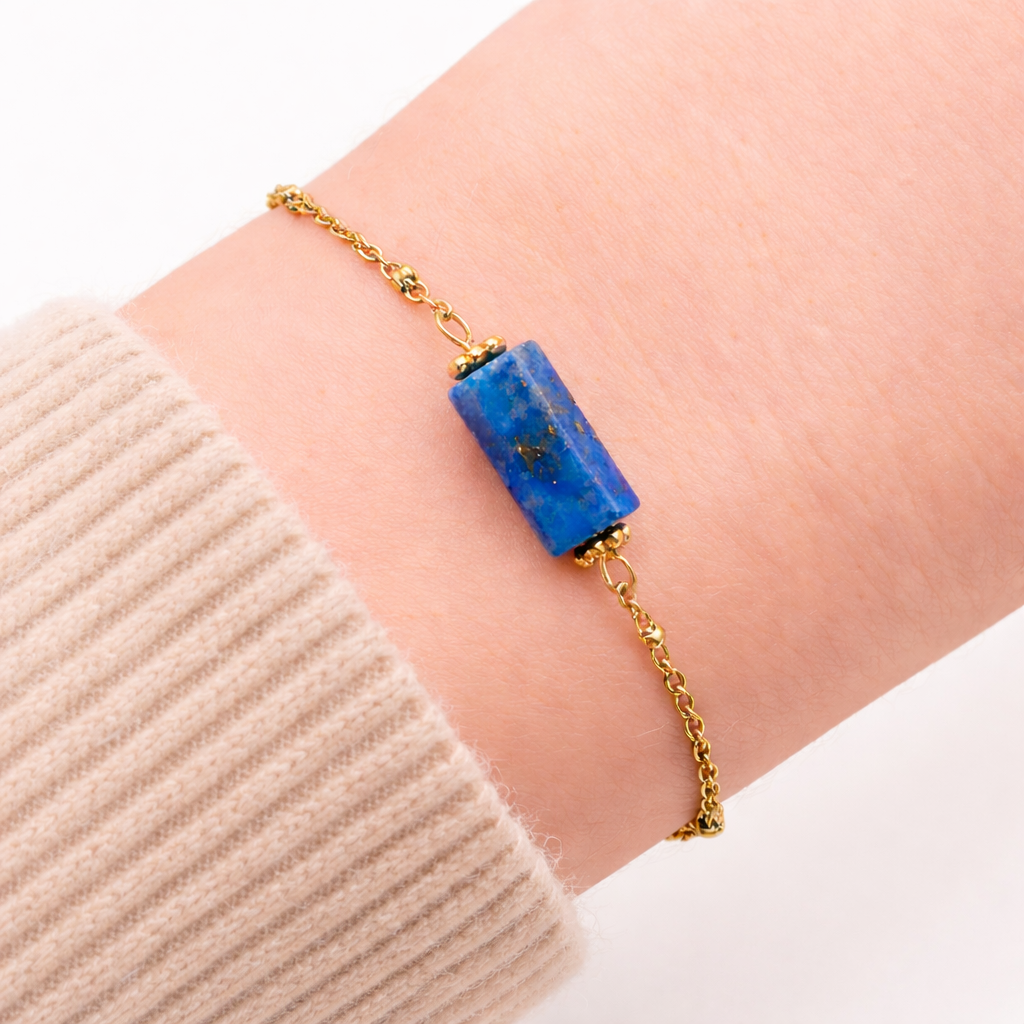 Bracelet chaine acier inoxydable doré et pierre centrale de lapis lazuli, porté sur un poignet avec pull ivoire