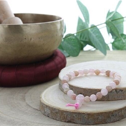 Brcalet pour enfant en pierres naturelles de quartz rose et de pierre de soleil, posé sur deux rondelles de bois, à c^ôté d'un bol tibétain