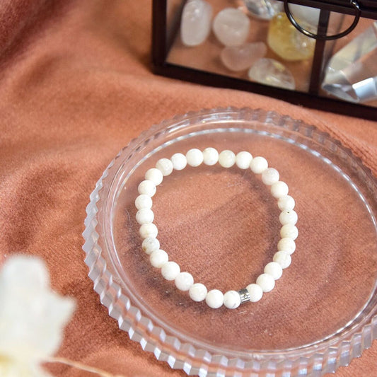 Bracelet en perles de pierre de lune blanche posé sur une coupelle en verre à côté d'une boite en verre contenant des cristaux