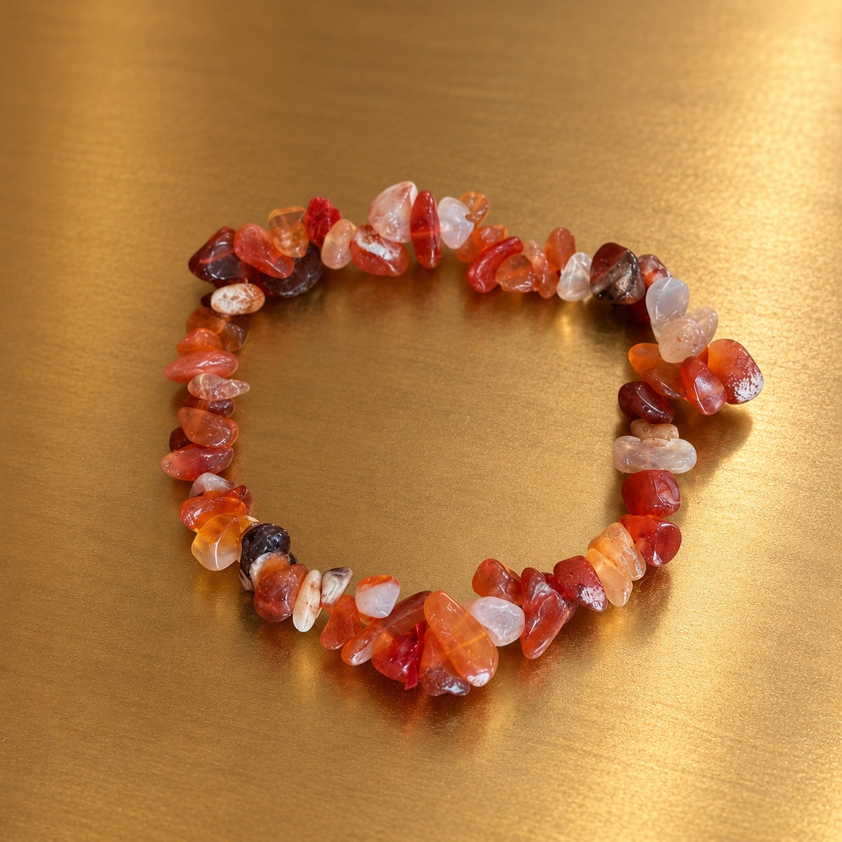 Bracelet en éclats de cornaline aux nuances orangées, rouges et translucides, disposé en cercle sur un fond doré