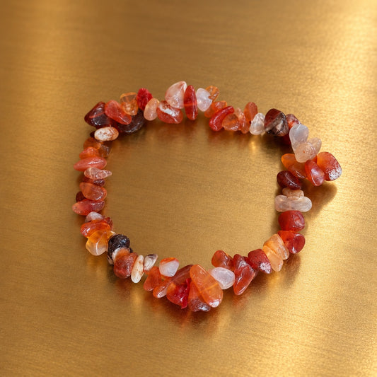 Bracelet en éclats de cornaline aux nuances orangées, rouges et translucides, disposé en cercle sur un fond doré