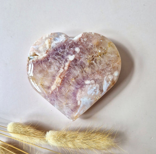 Coeur en améthyste rose drusée, posée sur un fond rose clair, accompagné de brins de pampas séchées