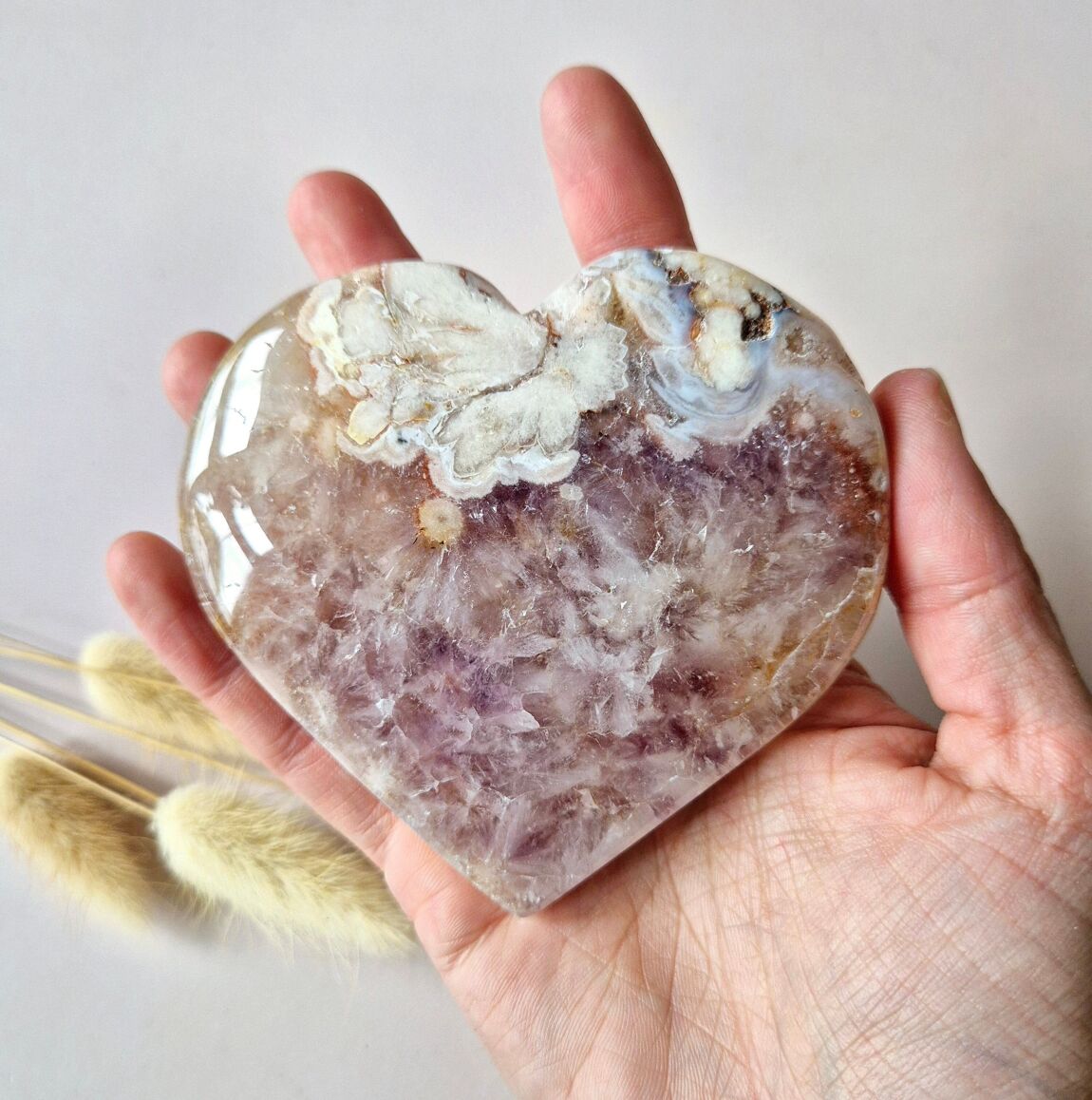 Main tenant un coeur en améthyste rose drusée, accompagné de brins de pampas séchées