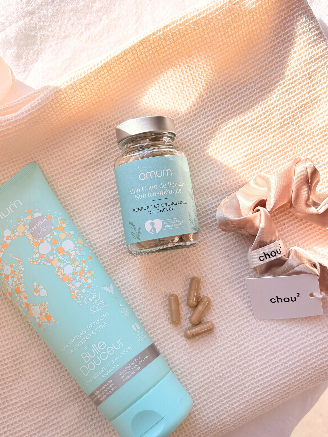 Tube de shampoing bleu lagon Omum, pot en verre de compléments alimentaires renfort et pousse du cheveu, 4 gélules,un chouchou satin doré sur tissu ivoire