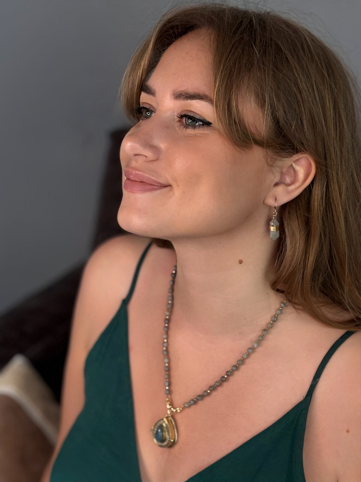 Femme portant un collier en perles de labradorite avec pendentif goutte serti doré et boucles d'oreilles assorties  De A à KÂ
