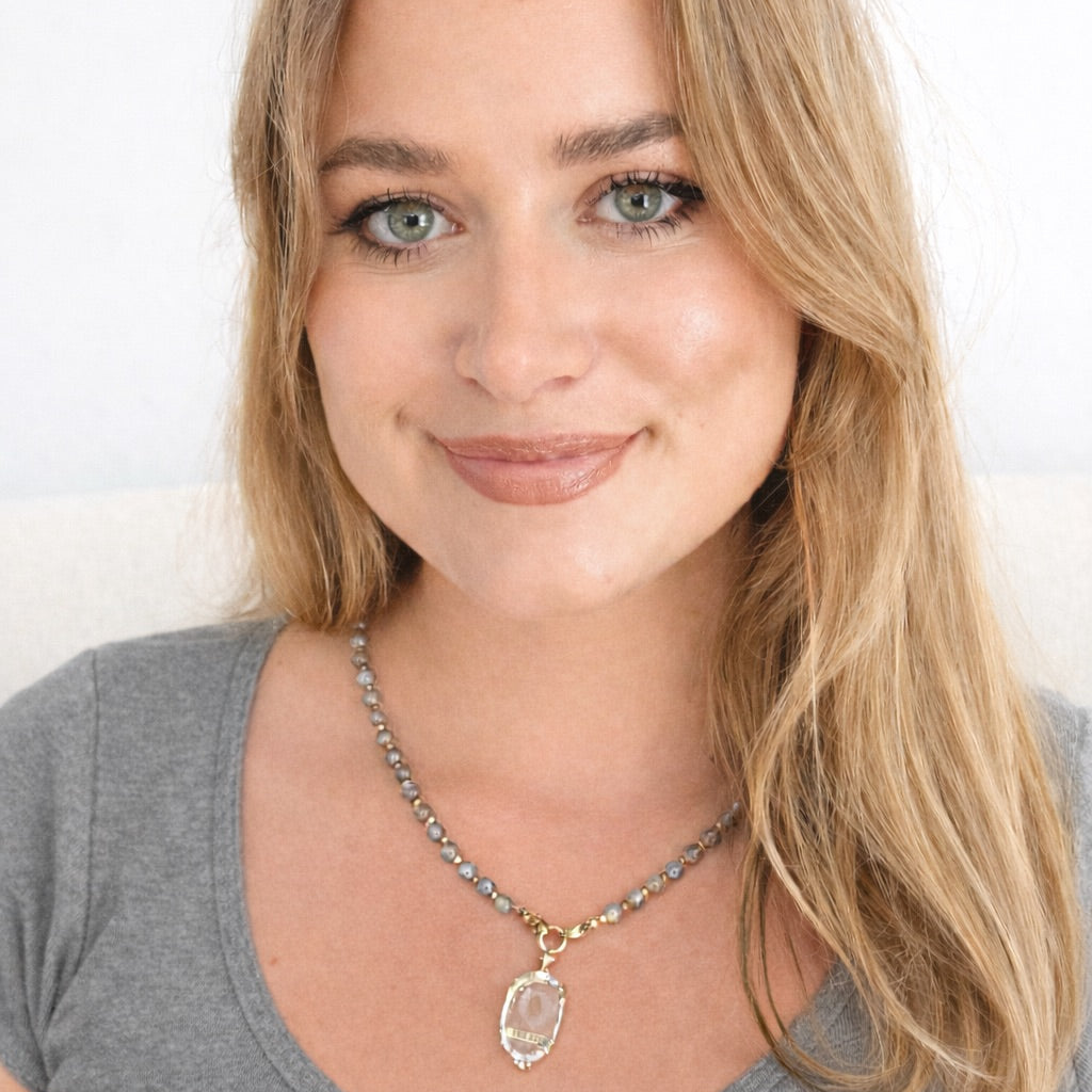 Femme blonde aux yeux verts portant un collier en perles de labradorite et son grigri pendentif en cristal de roche