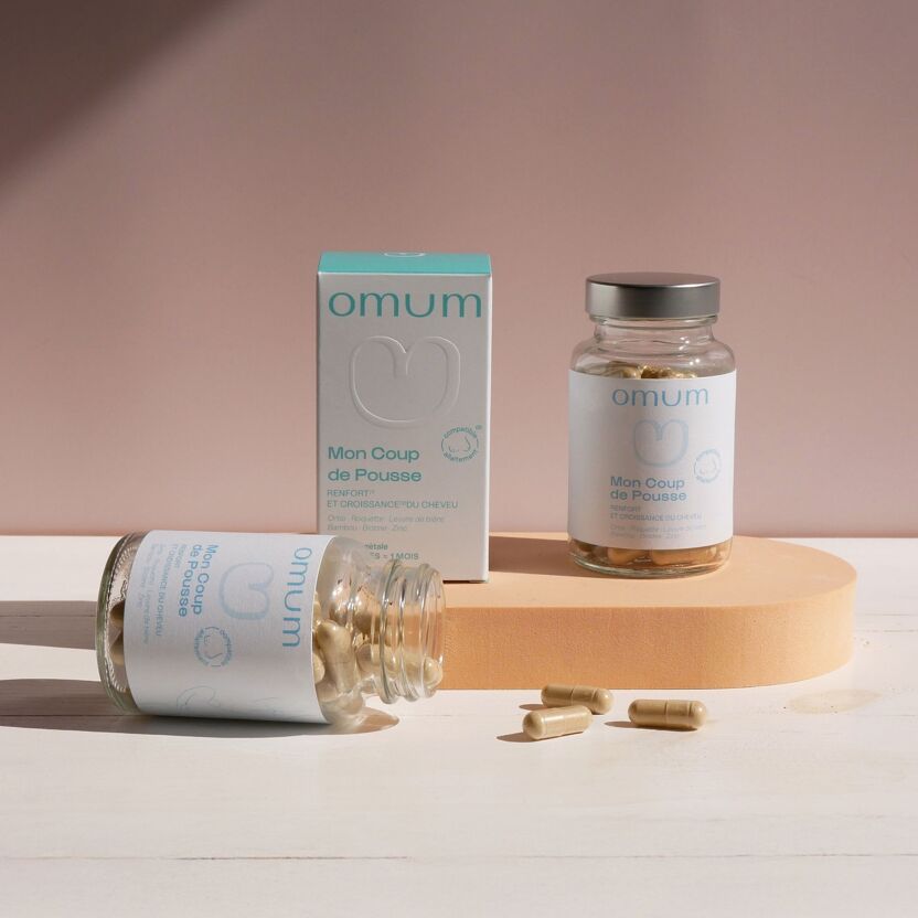 Compléments alimentaire pour cheveux Mon coup de pousse Omum présentés sur un plateau bois avec un flacon verre ouvert avec ses gélules et un flacon fermé et étui en carton blanc et bleu