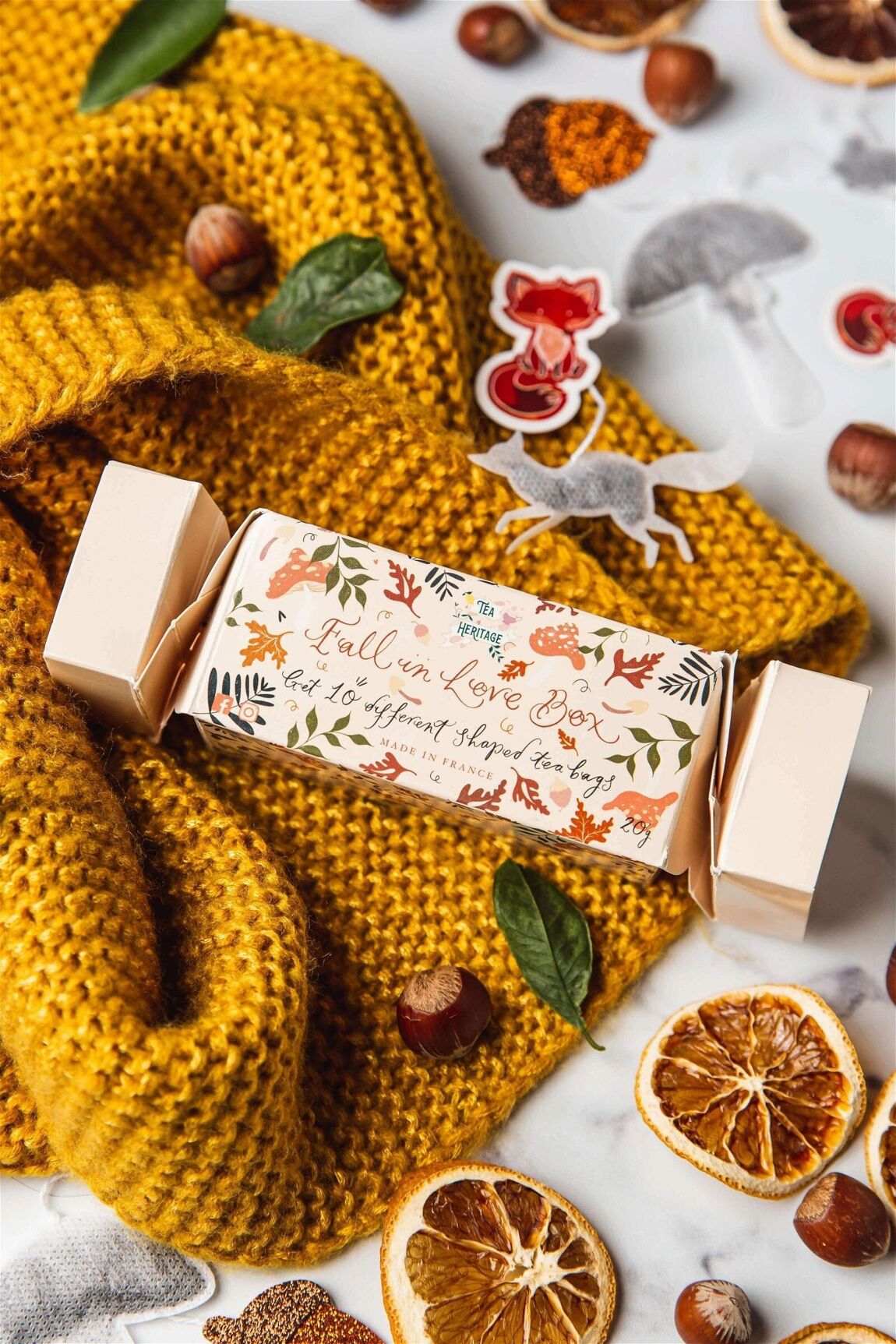 Pochette surprise façon crackers anglais contenant 10 thés biologiques, sur écharpe couleur moutarde, tranches d'oranges séchées, noisettes