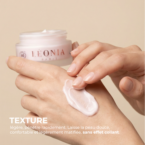 Mains de femme étalant la crème Léonia Paris, pot en verre dépoli, crème rose, logo certification bio, couvercle blanc et texte avec texture et ses propriétés