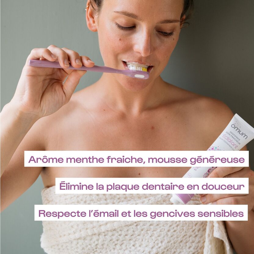 Femme se lavant les dents avec le dentifrice bio Omum L'Éclatant, tube blanc et bouchon violet, 3 titres des bienfaits de ce soin fraîcheur