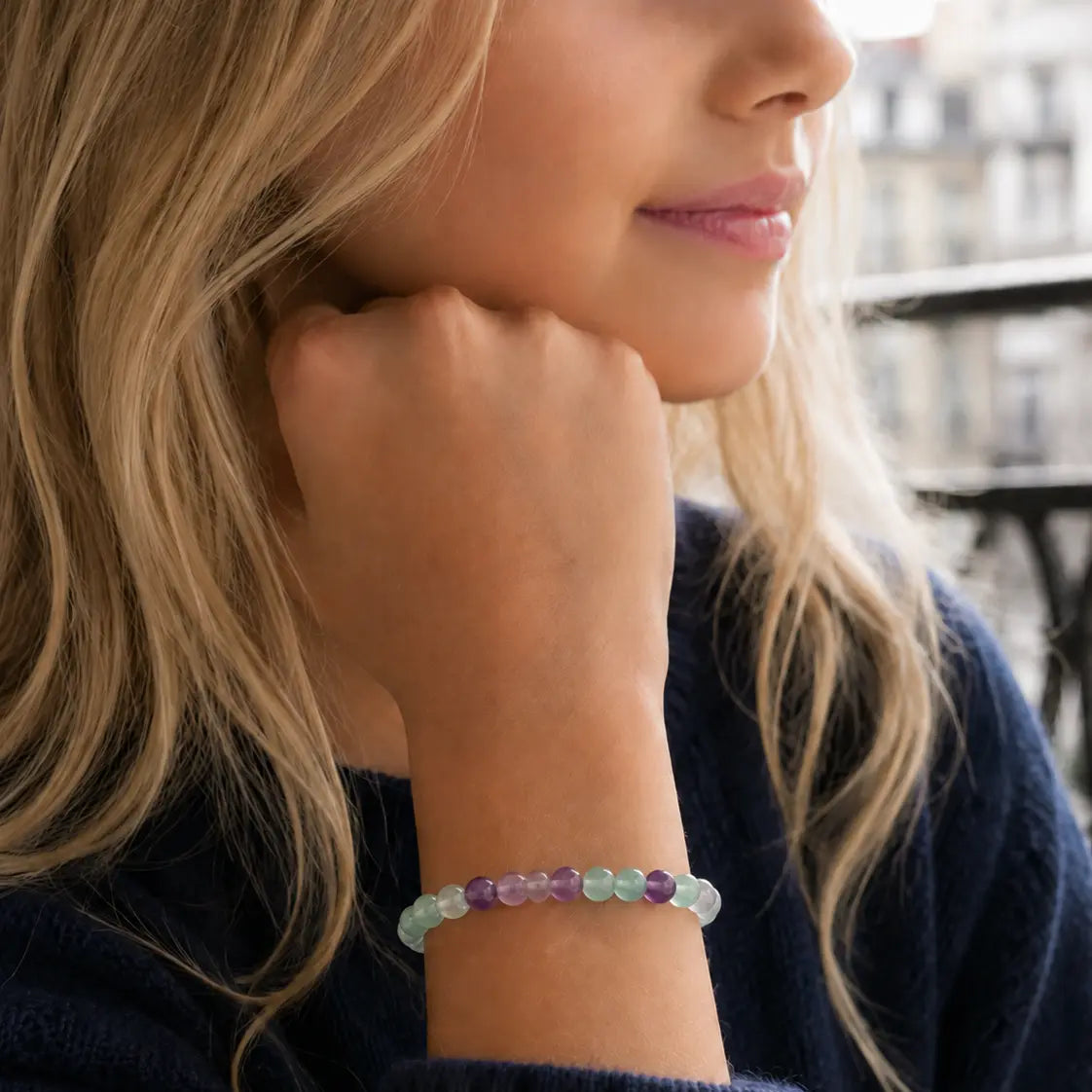 Fille portant un bracelet en perles de fluorite vertes et violettes au poignet, la main sous le menton
