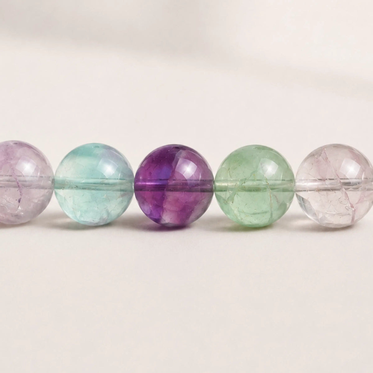Gros plan sur les perles rondes de fluorite translucides aux nuances vertes, violettes et mauves
