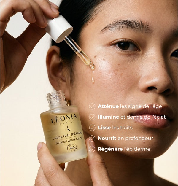 Femme appliquant l'Huile Pure Thé Blanc Bio Léonia Paris sur le visage avec pipette compte gouttes, texte atténue les signes de l'âge, illumine, lisse, nourrit et régénère l'épiderme