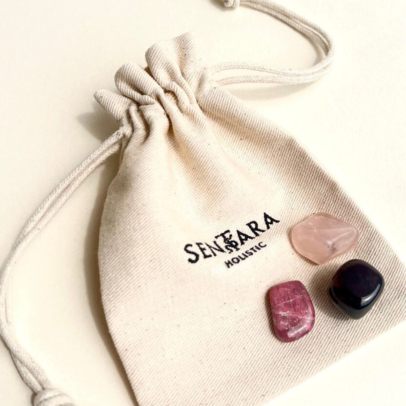 Kit amour de pierres roulées naturelles grenat rouge, quartz rose et rhodonite posées sur un pochon en coton ivoire avec Sentra Holistic en noir