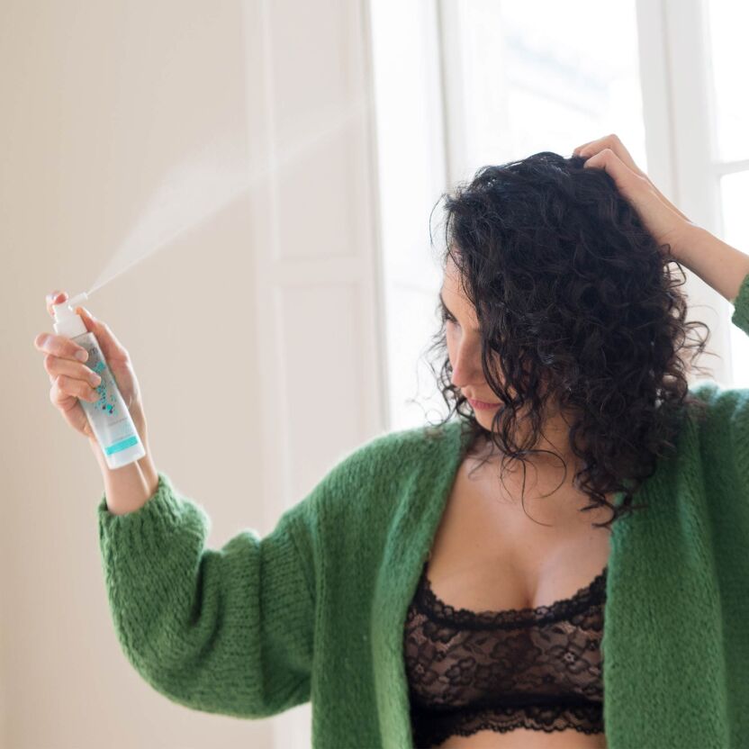 Femme en train de vaporiser sur ses cheveux la lotion anti-chute fortifiante Omum