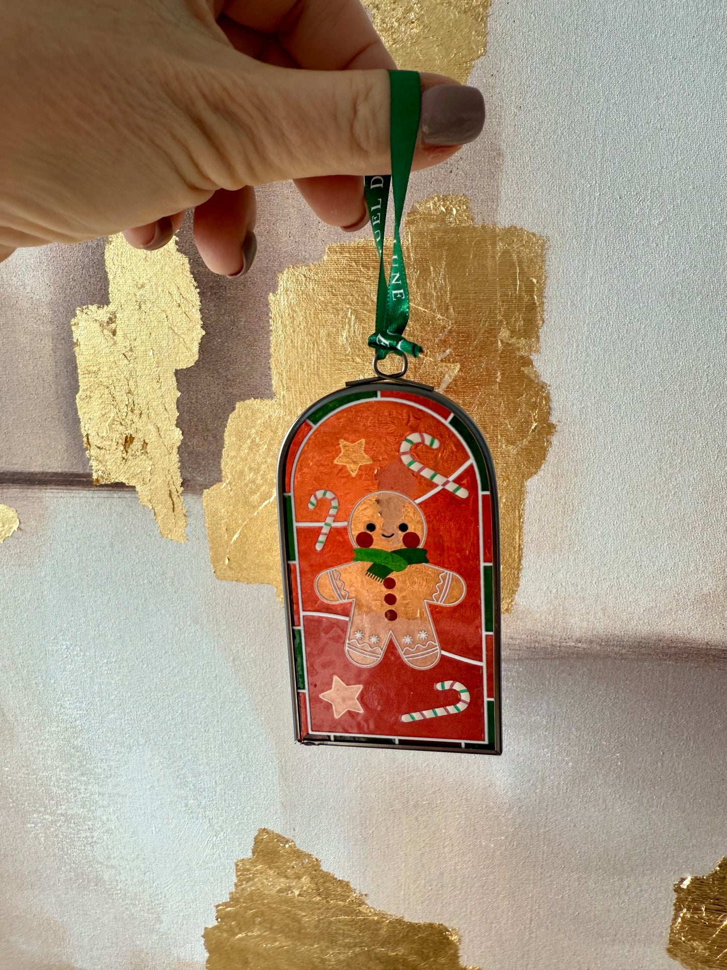 Main de femme tenant un vitrail au motif bonhomme pain d'épice avec ruban vert rituel de lune sur fond or et beige