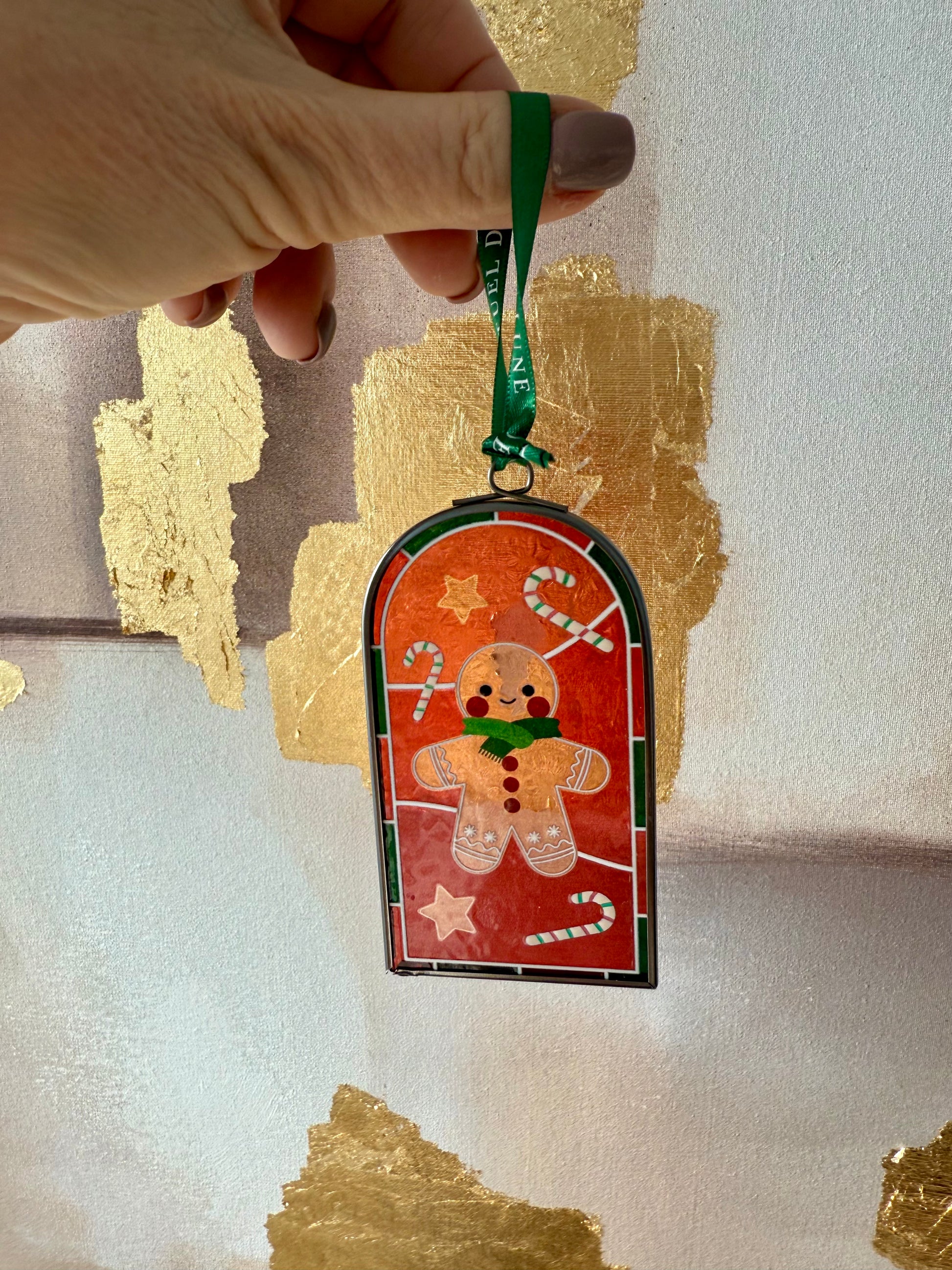 Main de femme tenant un vitrail au motif bonhomme pain d'épice avec ruban vert rituel de lune sur fond or et beige