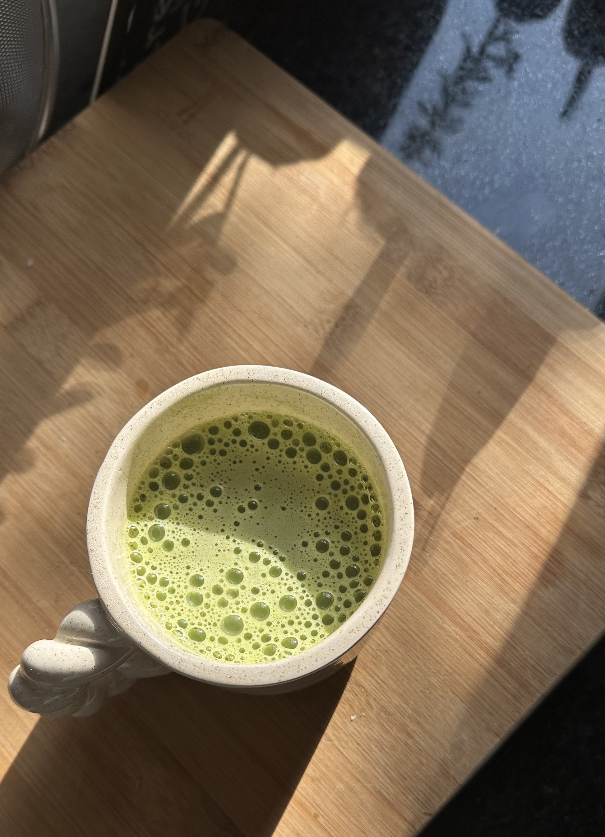 Photo d'ambiance d'une tasse de thé matcha en grés sur une planche en bois et rayon de lumière