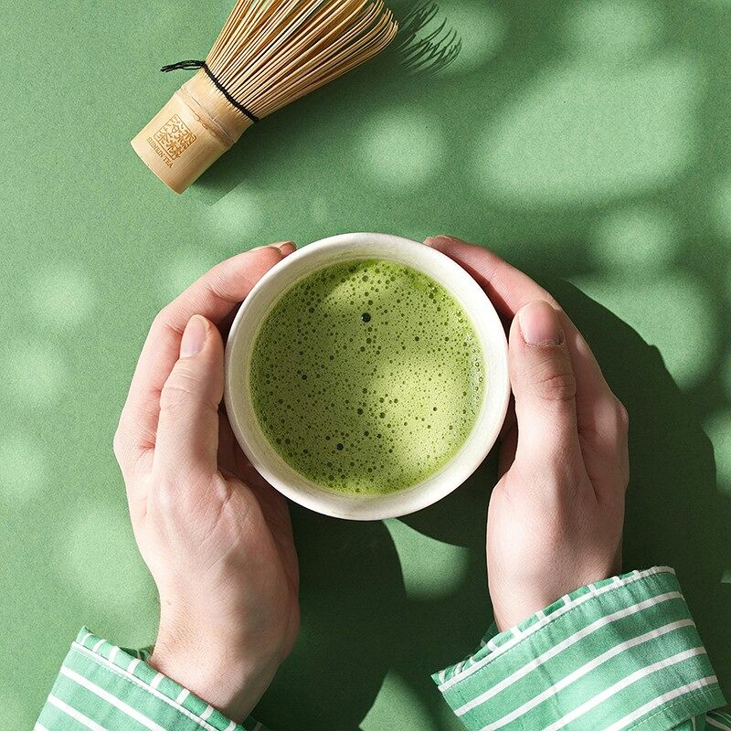 Bol de thé matcha dans les mains, à côté de son fouet à matcha, chasen