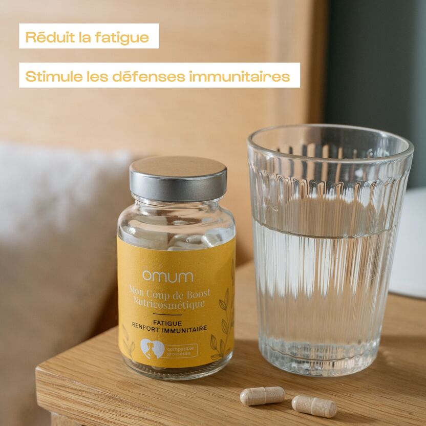 Visuel d'un flacon de compléments alimentaires Omum Mon coup de boost posé à côté d'un verre d'eau et ses 2 gélules, ambiance zen, et ses bienfaits