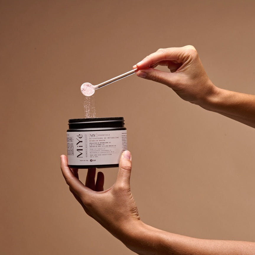 Main de femme tenant le pot Activateur de Métabolisme MiYé avec cuillère doseuse , texture poudre complément alimentaire régulation hormonale